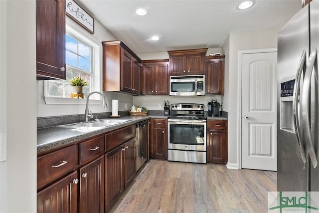 kitchen with light wood-type flooring, a sink, dark countertops, recessed lighting, and appliances with stainless steel finishes