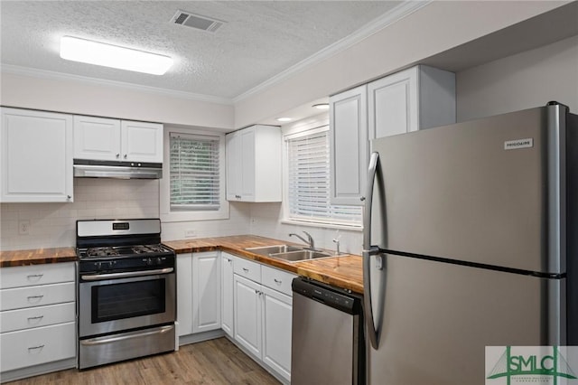 kitchen featuring under cabinet range hood, appliances with stainless steel finishes, white cabinetry, wood counters, and a sink