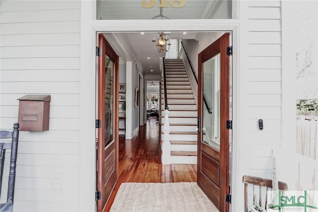 foyer with crown molding, stairs, an inviting chandelier, and wood finished floors