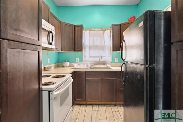 kitchen featuring stainless steel microwave, light countertops, freestanding refrigerator, white electric range oven, and a sink