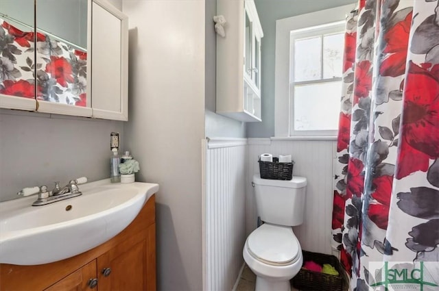 full bath featuring a shower with curtain, vanity, toilet, and wainscoting