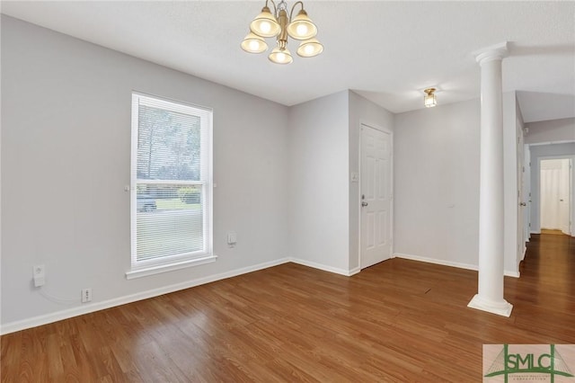 spare room featuring a chandelier, baseboards, and wood finished floors