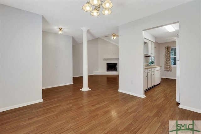 unfurnished living room with a fireplace with raised hearth, baseboards, lofted ceiling, ceiling fan with notable chandelier, and wood finished floors