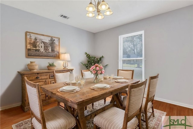 dining area featuring a notable chandelier, visible vents, baseboards, and wood finished floors