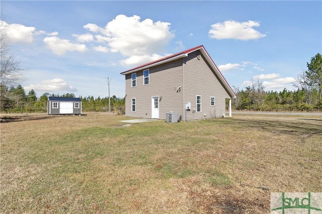 back of property with an outbuilding, central air condition unit, a storage unit, and a lawn