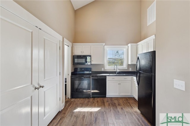 kitchen with white cabinetry, black appliances, a towering ceiling, and a sink