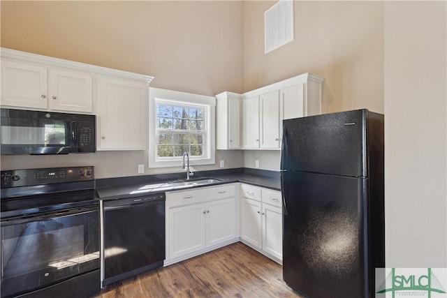 kitchen with dark countertops, visible vents, white cabinets, black appliances, and a sink