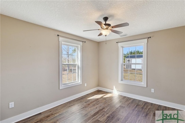 spare room featuring a wealth of natural light, dark wood finished floors, a ceiling fan, and baseboards