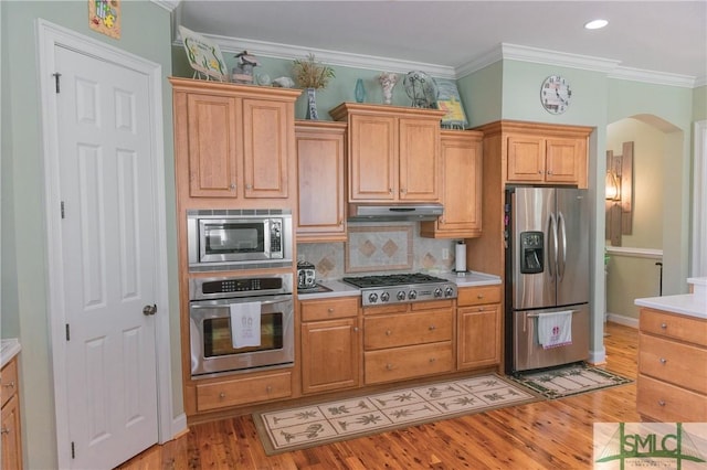 kitchen featuring under cabinet range hood, stainless steel appliances, arched walkways, and light countertops