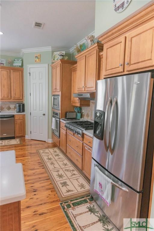 kitchen featuring visible vents, crown molding, under cabinet range hood, light wood-style flooring, and appliances with stainless steel finishes