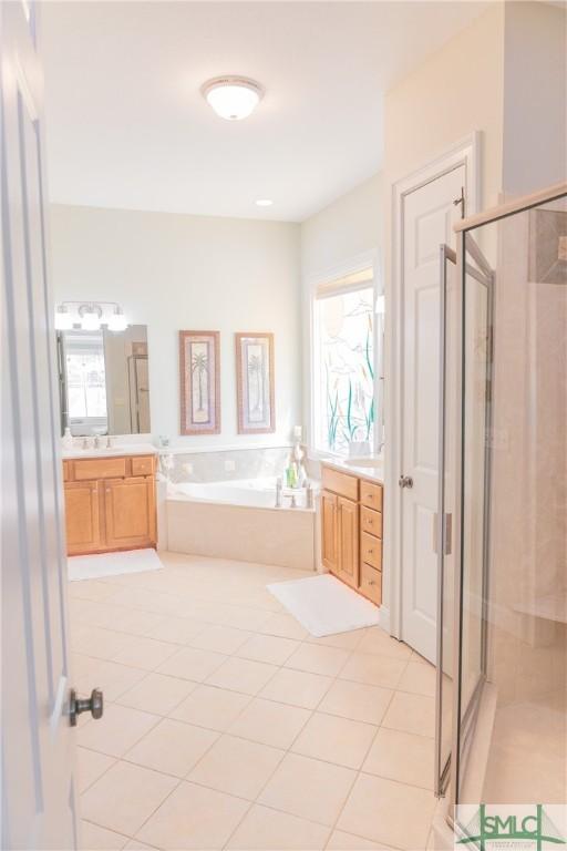 bathroom featuring a bath, a shower stall, tile patterned floors, and two vanities