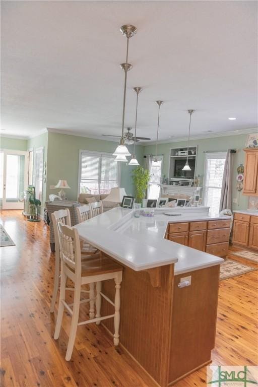 kitchen featuring crown molding, ceiling fan, pendant lighting, a breakfast bar, and light wood-style flooring