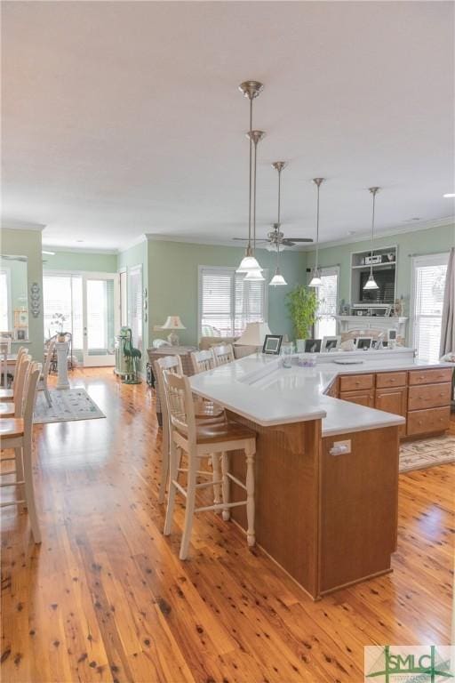 kitchen featuring a kitchen bar, light wood-style floors, crown molding, light countertops, and ceiling fan