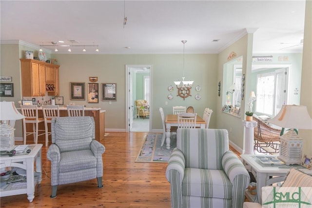 living area with light wood-style floors, baseboards, a chandelier, and ornamental molding