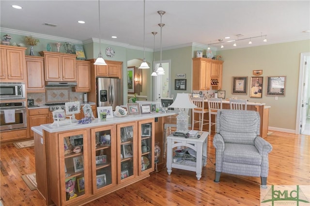 kitchen with under cabinet range hood, a center island, appliances with stainless steel finishes, light countertops, and decorative backsplash