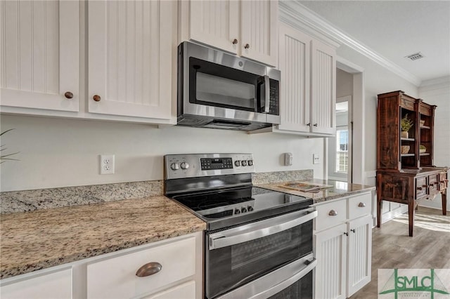 kitchen with stainless steel appliances, light stone countertops, crown molding, and white cabinetry