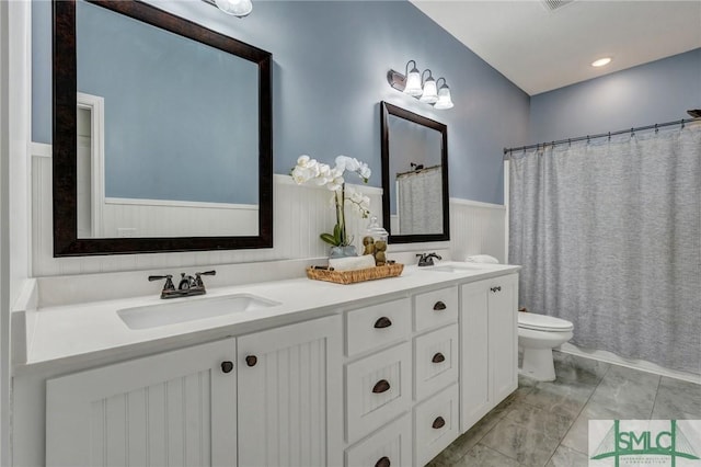 bathroom featuring double vanity, toilet, and a sink