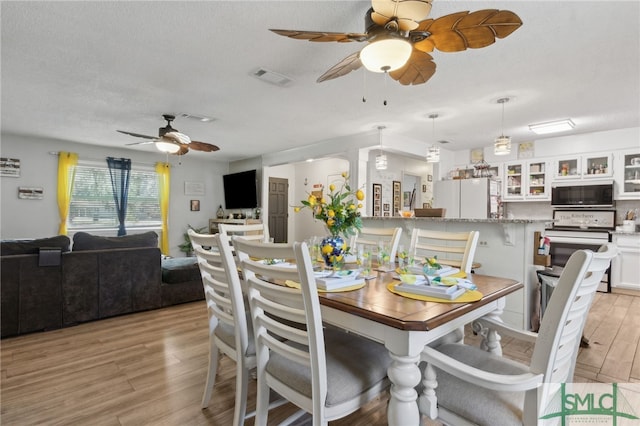 dining space featuring visible vents, light wood-style floors, a ceiling fan, and a textured ceiling