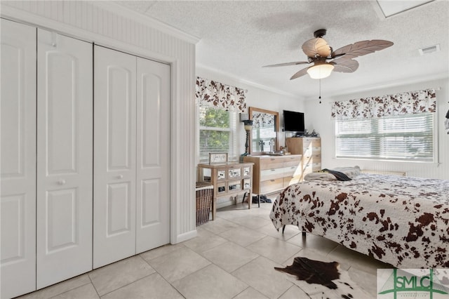 bedroom with visible vents, a textured ceiling, a closet, crown molding, and light tile patterned floors