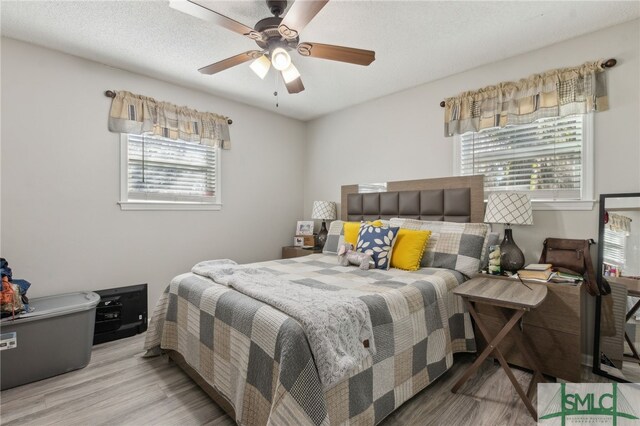 bedroom with multiple windows, a textured ceiling, ceiling fan, and wood finished floors