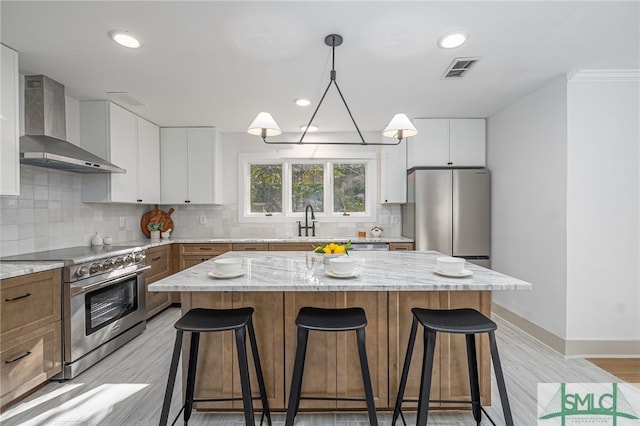 kitchen featuring stainless steel appliances, visible vents, a breakfast bar, and wall chimney range hood