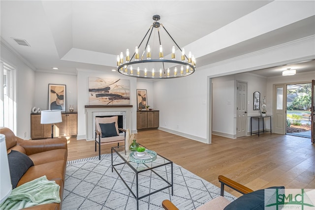 living room with visible vents, a notable chandelier, light wood-style flooring, crown molding, and a raised ceiling