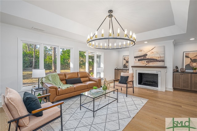 living area with visible vents, a tray ceiling, wood finished floors, a fireplace, and a chandelier