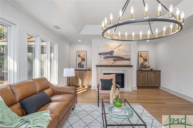 living area featuring visible vents, ornamental molding, wood finished floors, a high end fireplace, and an inviting chandelier