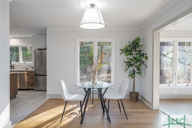 dining area featuring light wood finished floors, visible vents, crown molding, and baseboards