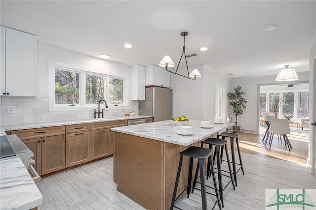 kitchen featuring light stone countertops, a breakfast bar area, brown cabinets, freestanding refrigerator, and a sink