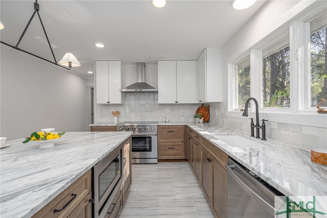 kitchen with backsplash, light stone counters, stainless steel appliances, wall chimney exhaust hood, and a sink