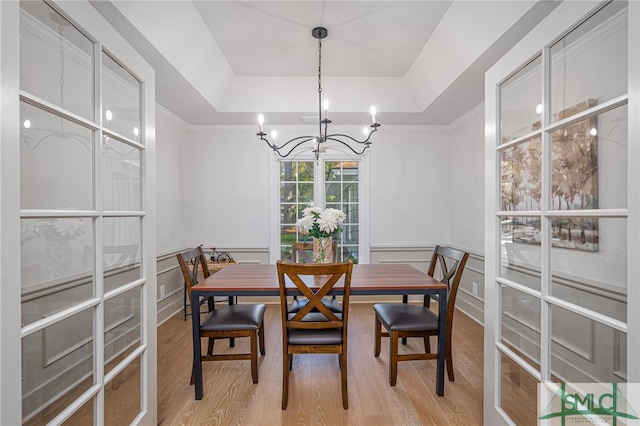 dining room with light wood-style flooring, wainscoting, a decorative wall, a raised ceiling, and a chandelier