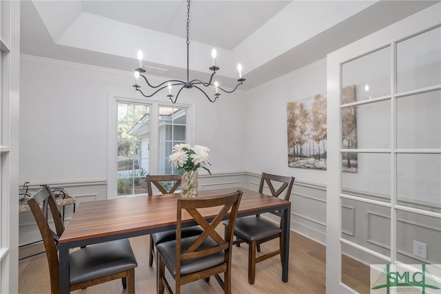 dining space featuring an inviting chandelier, a tray ceiling, a decorative wall, and light wood finished floors