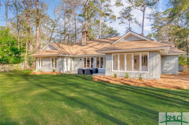 back of house featuring board and batten siding, a chimney, a yard, and a sunroom