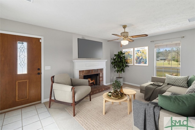 living area with light tile patterned floors, a fireplace, baseboards, and a ceiling fan