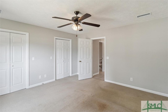 unfurnished bedroom with carpet flooring, baseboards, visible vents, and two closets