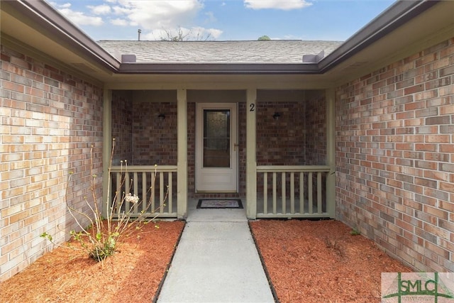 entrance to property featuring brick siding, a porch, and roof with shingles