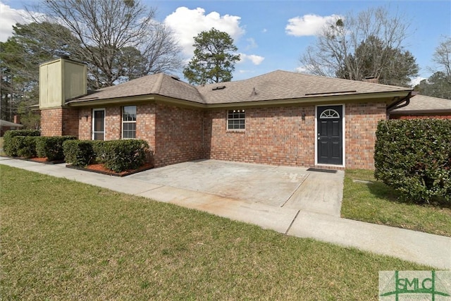 ranch-style house featuring roof with shingles, a front yard, brick siding, a chimney, and a patio area