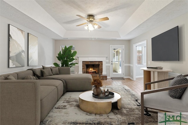 living area featuring light wood finished floors, a textured ceiling, a raised ceiling, and ceiling fan