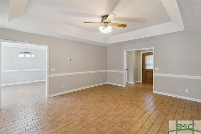 spare room with light wood finished floors, ceiling fan with notable chandelier, baseboards, and a tray ceiling