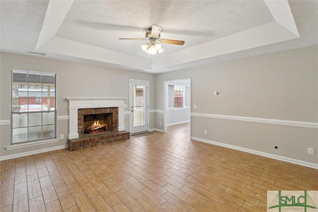 unfurnished living room featuring a tray ceiling, a textured ceiling, visible vents, and light wood-style flooring