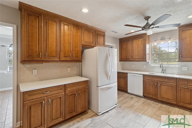 kitchen with brown cabinetry, visible vents, white appliances, and a sink