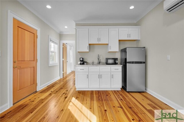 114 W Bolton St, Savannah, GA 31401 - kitchen featuring freestanding refrigerator, an AC wall unit, black microwave, white cabinets, and ornamental molding