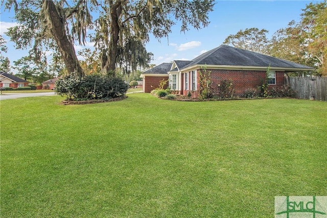 view of side of home featuring brick siding, a lawn, and fence