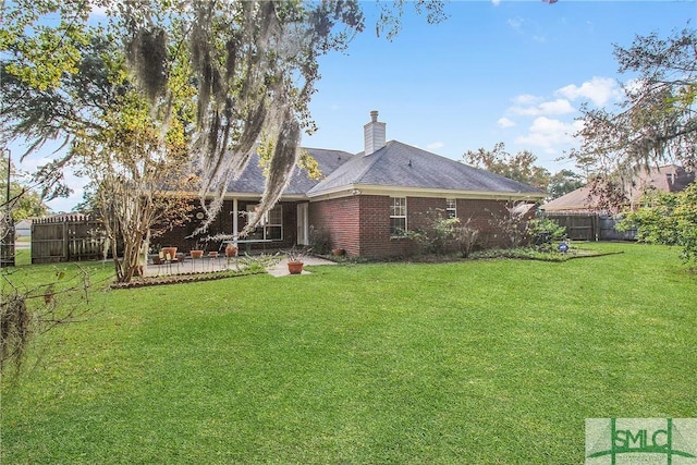 rear view of house with brick siding, a lawn, a chimney, a fenced backyard, and a patio