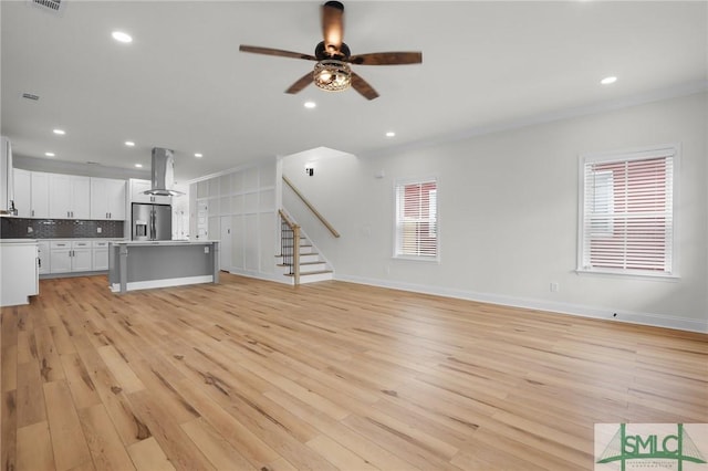 unfurnished living room featuring stairway, a ceiling fan, baseboards, light wood-style flooring, and recessed lighting