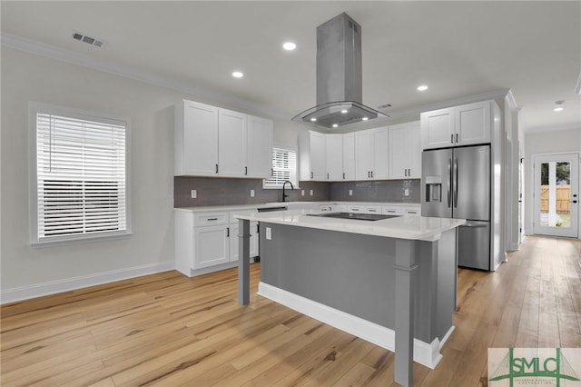 kitchen featuring visible vents, stainless steel fridge, island range hood, light countertops, and black electric stovetop