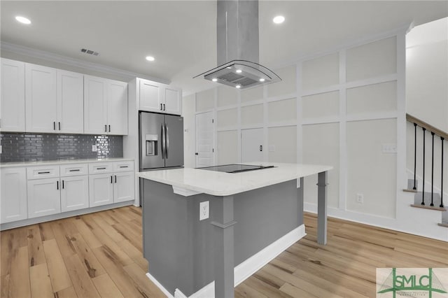 kitchen featuring visible vents, stainless steel fridge with ice dispenser, light countertops, island exhaust hood, and a decorative wall