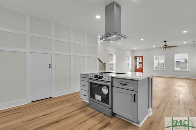 kitchen with stainless steel electric range oven, gray cabinets, light wood-style flooring, island exhaust hood, and a decorative wall