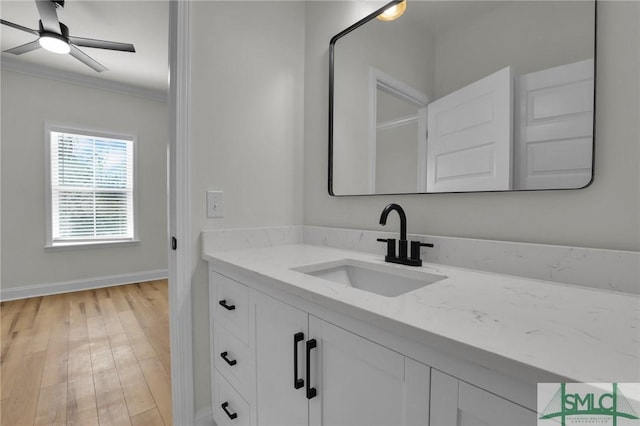 bathroom with a ceiling fan, wood finished floors, crown molding, baseboards, and vanity